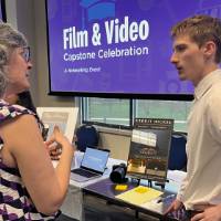 Event attendee chatting with student at their booth